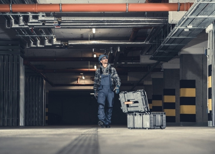 plumbing technician walking along underground parking with his toolbox looking for leaks.