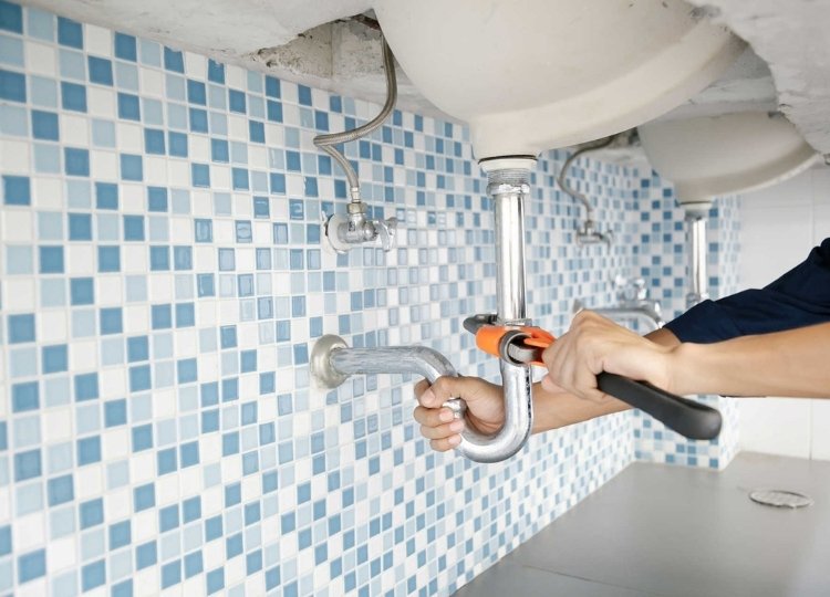 Plumber’s hands on close up working on bathroom sink with wrench on hand